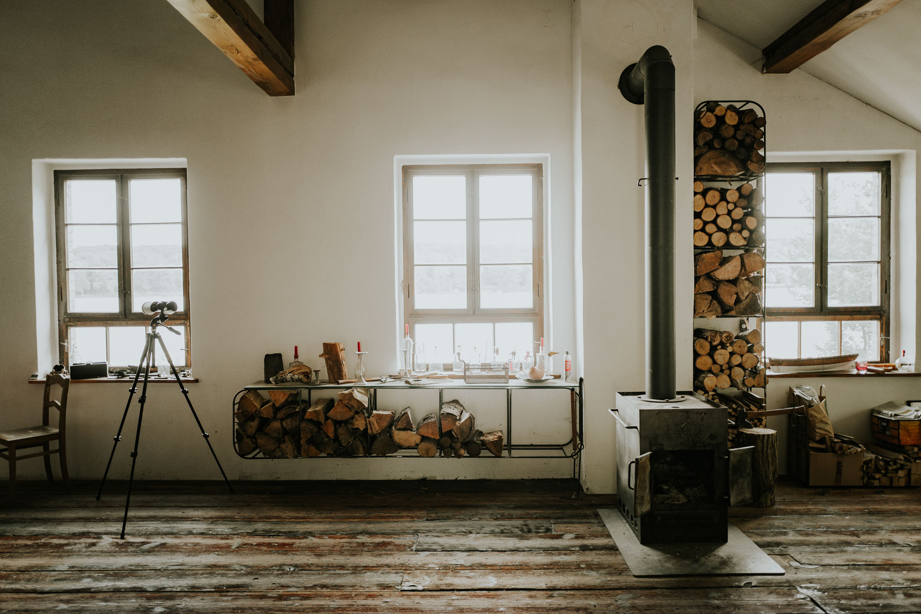 zeigt Raum schickes Innendesign mit Kamin Holzdielung Holzscheite Spektiv Fenster @ SASCHA HOECKER