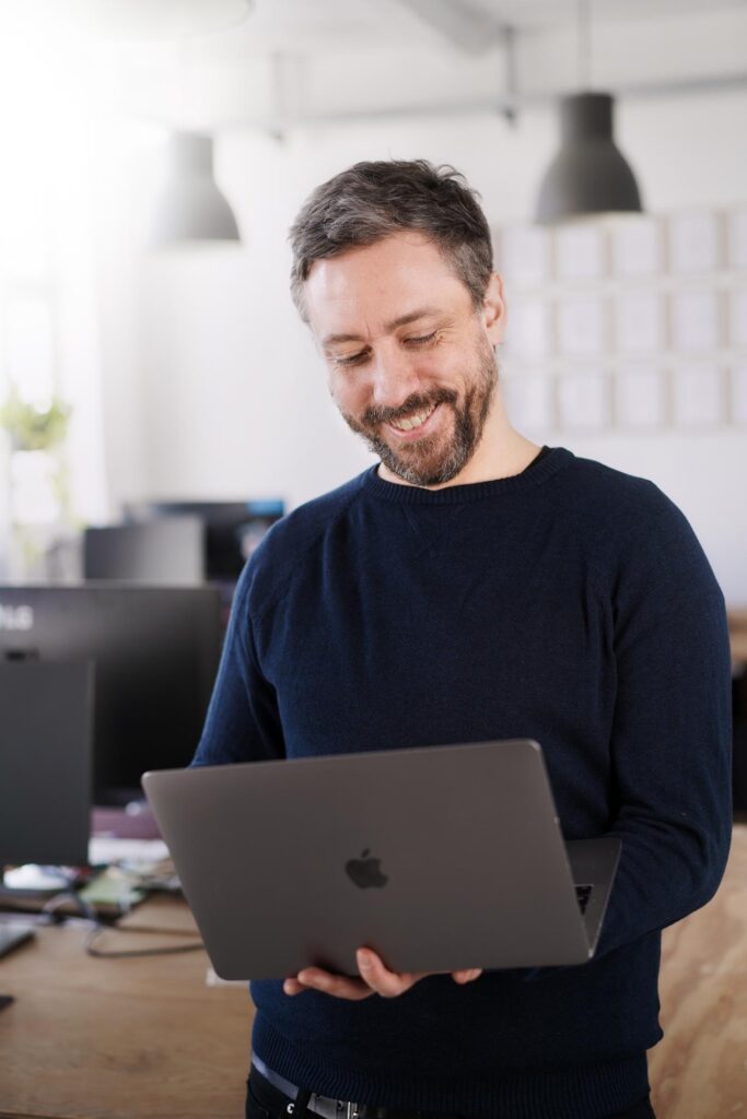 Corporate Portrait eines Mannes mit Laptop stehend in einem hellen modernen CoWorking Space.