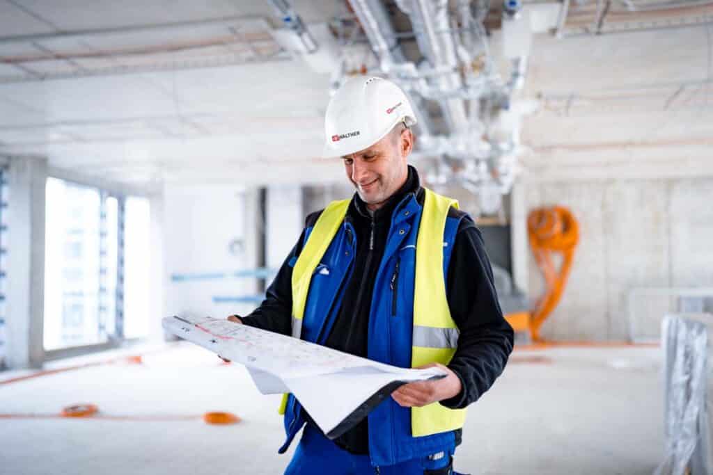 Employer Branding Fotografie für IB Walther: Mitarbeiter mit Helm und Warnweste liest einen Bauplan auf einer Baustelle in Berlin